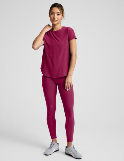 Woman in a magenta t-shirt and leggings outfit against a plain background.