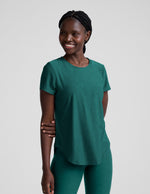Woman wearing a green t-shirt and leggings against a plain background.
