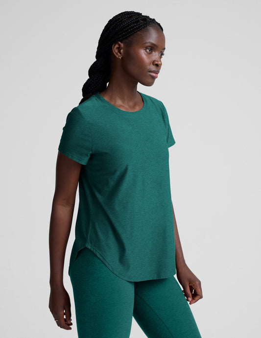 Woman wearing a green t-shirt and leggings against a plain background.