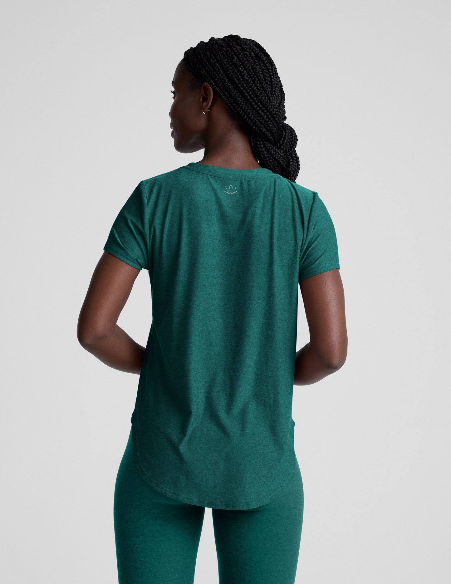 Woman wearing a green t-shirt and leggings against a plain background.