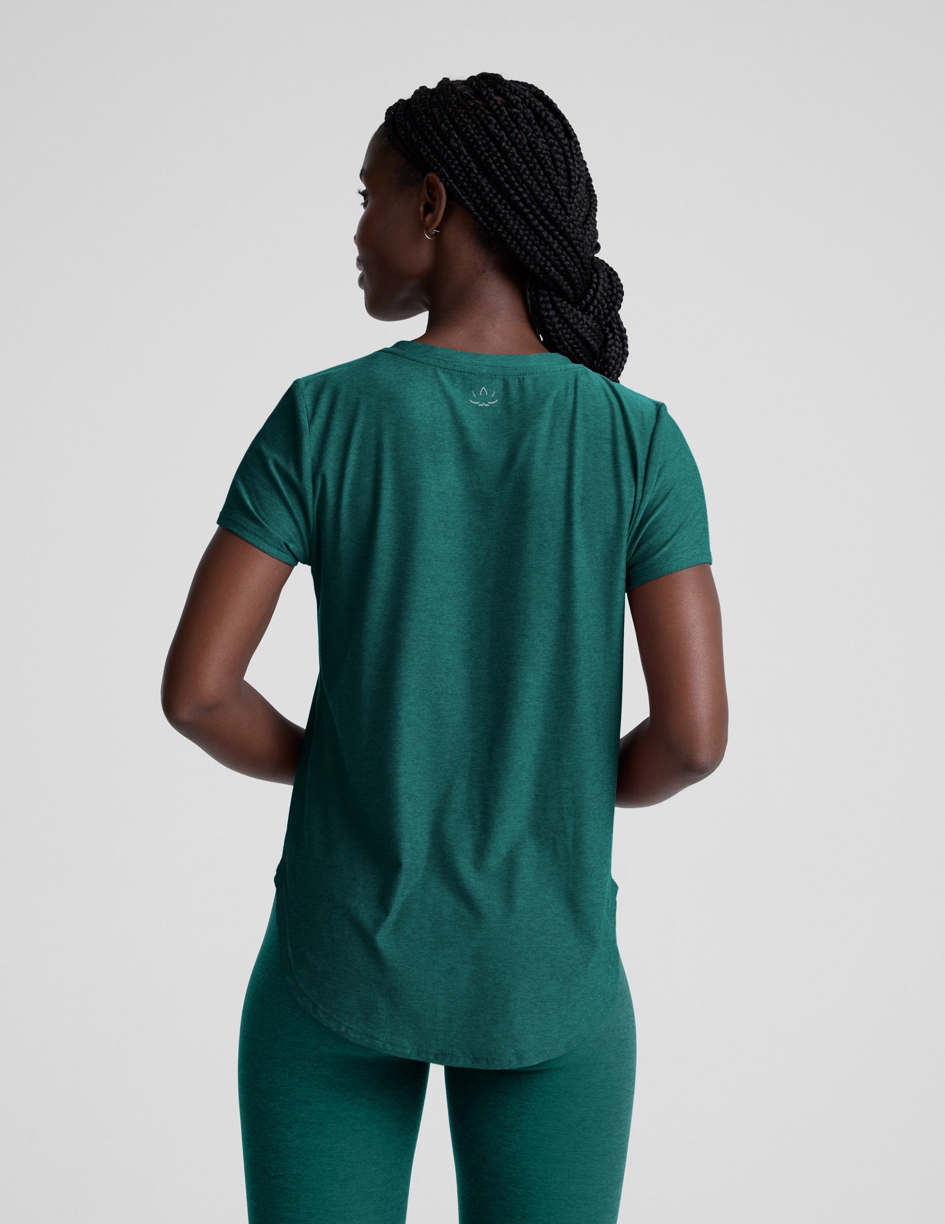 Woman wearing a green t-shirt and leggings against a plain background.