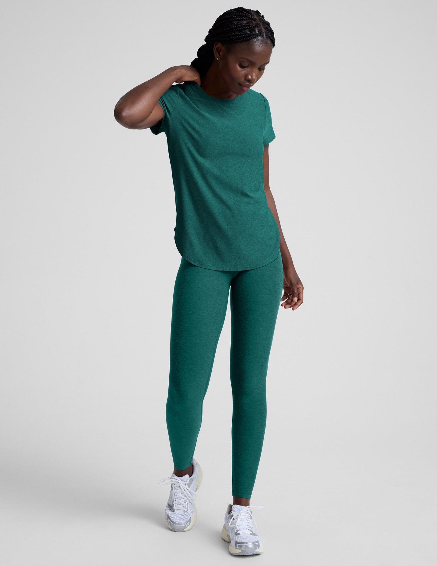 Woman wearing a green t-shirt and leggings against a plain background.