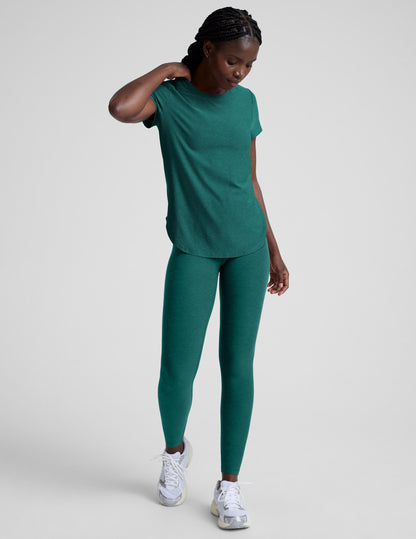 Woman wearing a green t-shirt and leggings against a plain background.