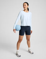 Woman wearing a light blue long sleeve and navy blue biker shorts against a plain background.