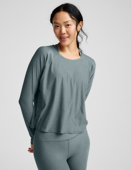 Woman wearing a green long sleeve and leggings against a plain background.