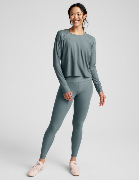 Woman wearing a green long sleeve and leggings against a plain background.