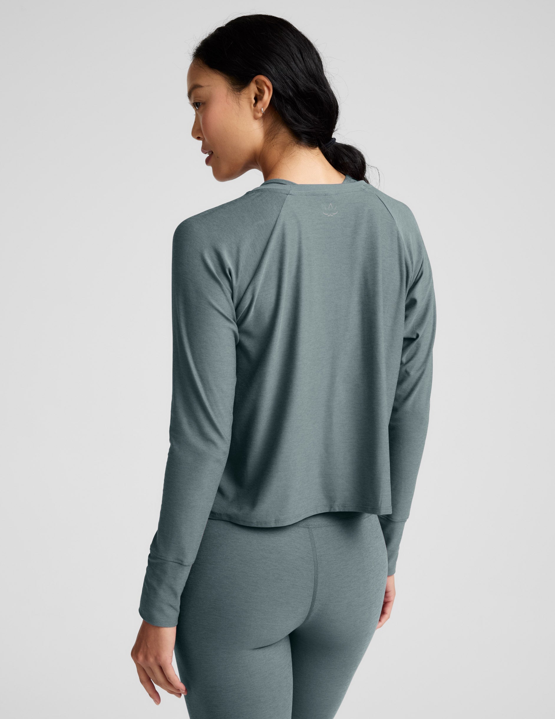 Woman wearing a green long sleeve and leggings against a plain background.