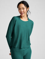 Woman wearing a teal long-sleeve top and leggings on a light gray background.