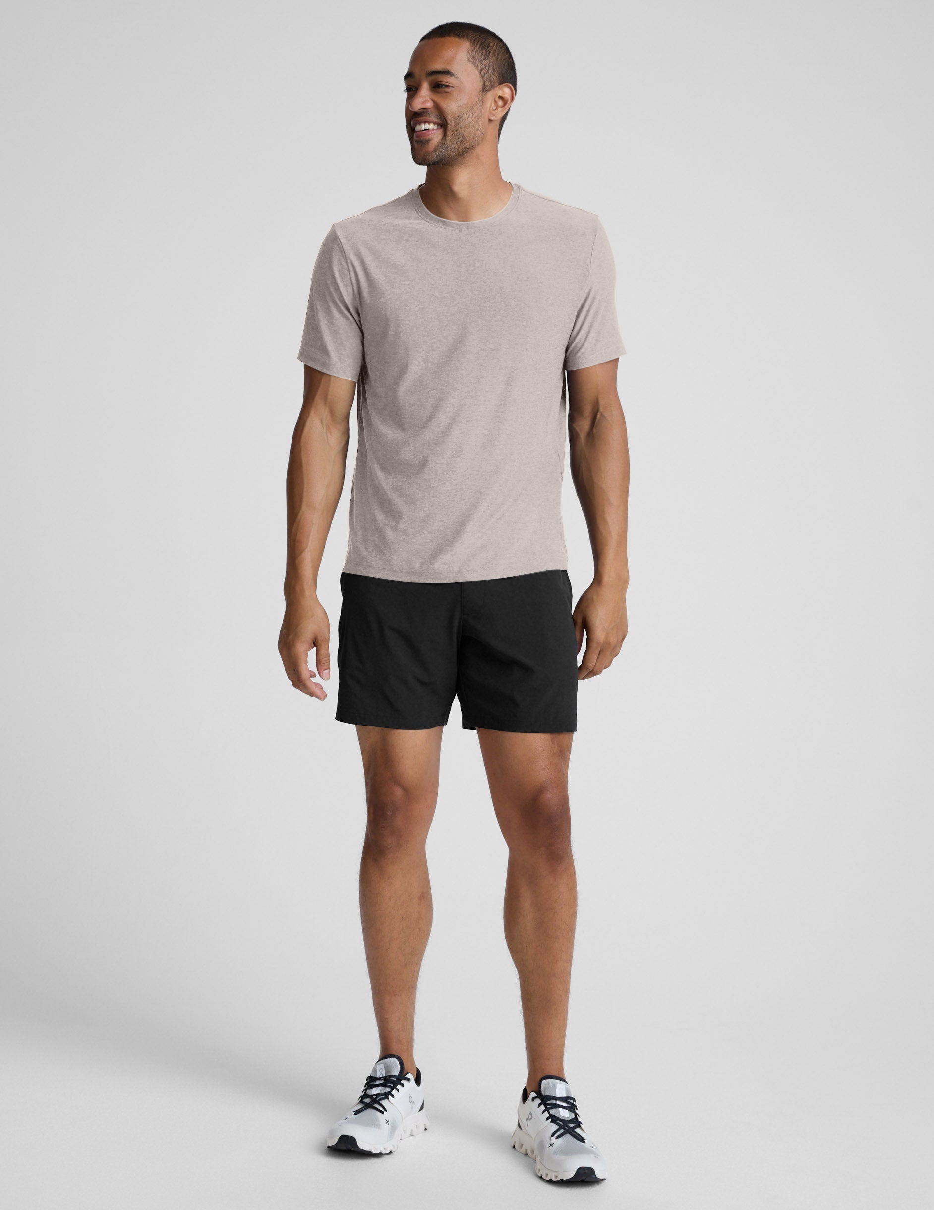 Man wearing a beige t-shirt and black shorts against a plain background.
