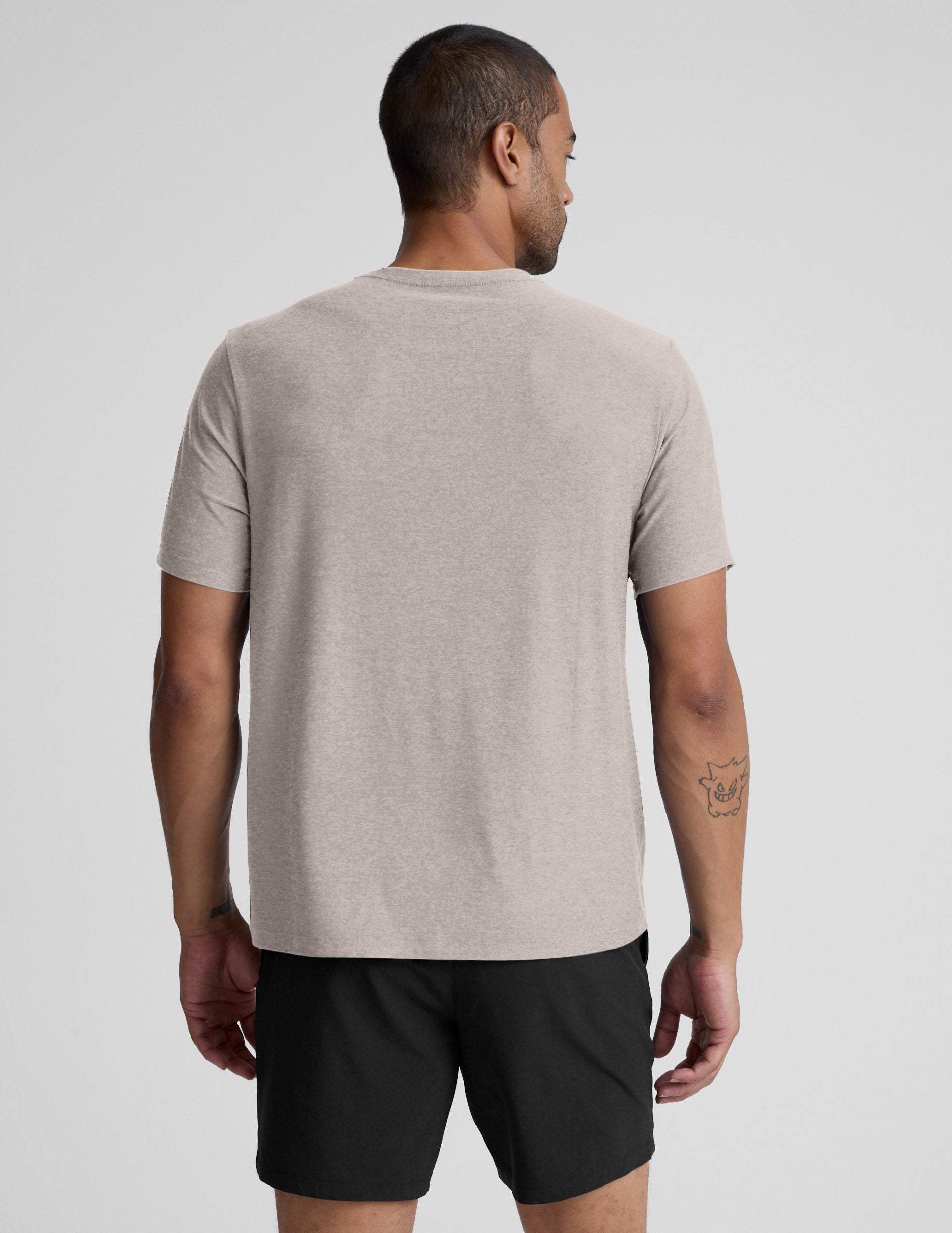 Man wearing a beige t-shirt and black shorts against a plain background.