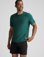 Man wearing a green t-shirt and black shorts on a light gray background.