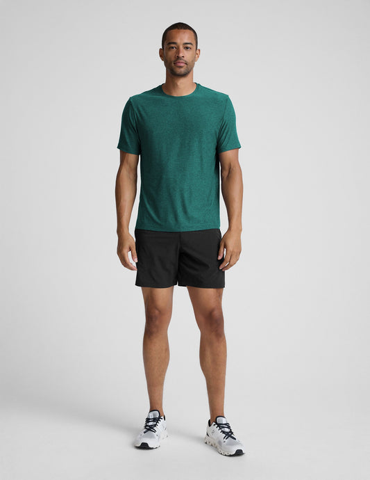 Man wearing a green t-shirt and black shorts on a light gray background.