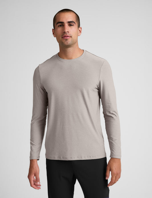 Man wearing a beige long-sleeve shirt and black pants against a plain background.