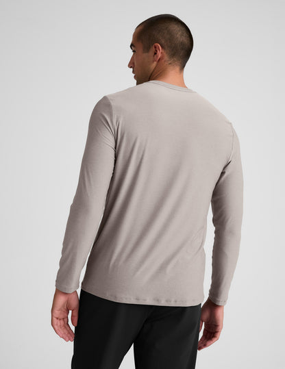 Man wearing a beige long-sleeve shirt and black pants against a plain background.
