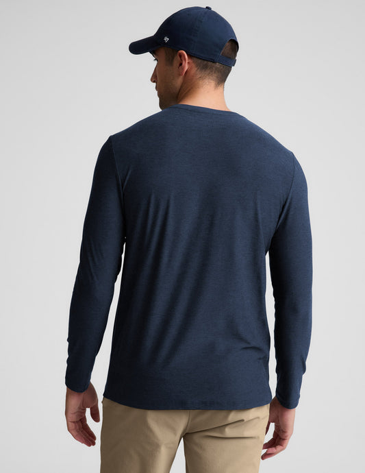 Man wearing a navy long sleeve shirt and khaki pants against a plain background.