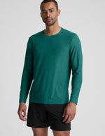 Man wearing a green long sleeve top and black shorts against a light grey background.