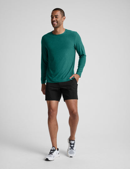 Man wearing a green long sleeve top and black shorts against a light grey background.