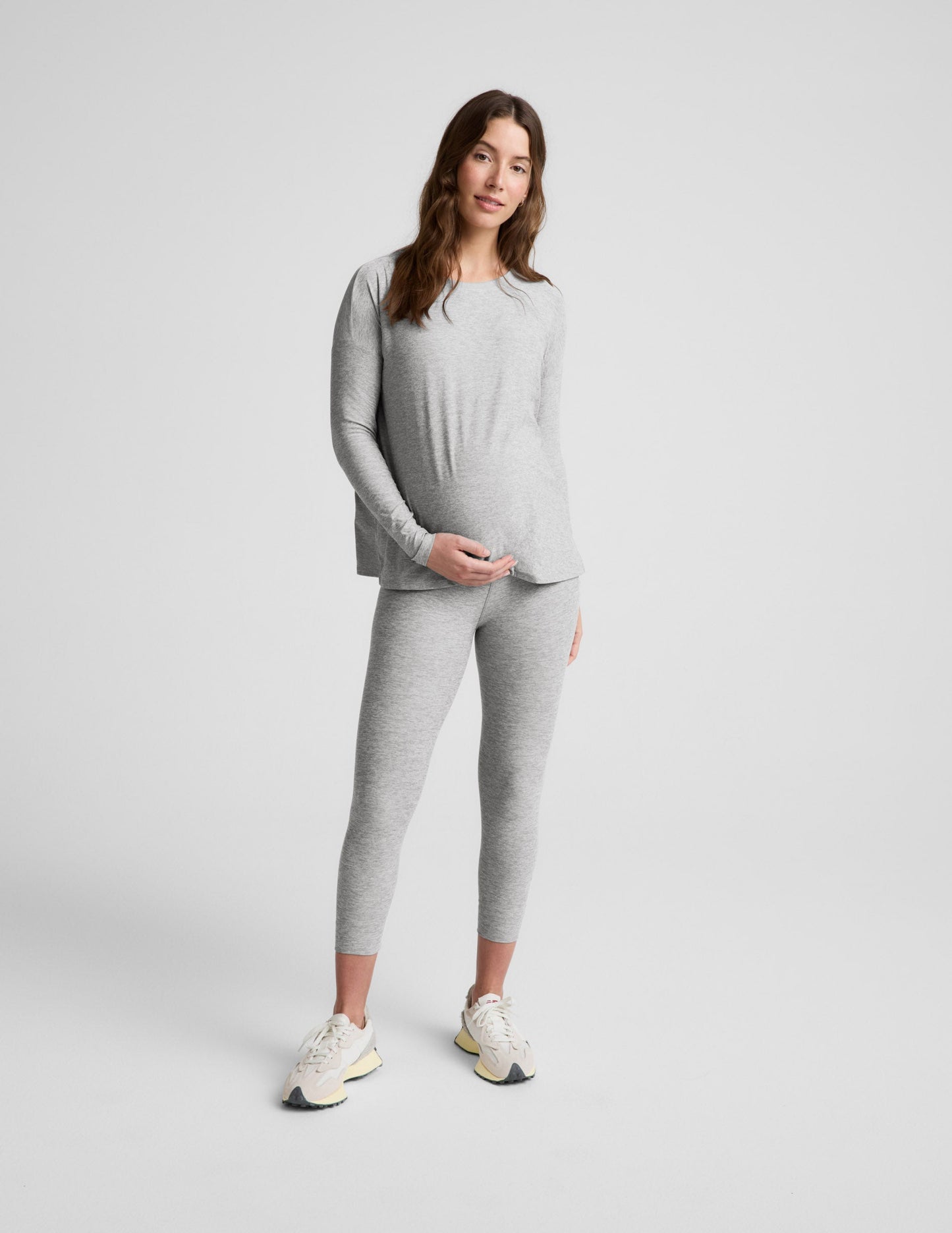 Pregnant woman wearing a gray long-sleeve top and leggings on a white background.
