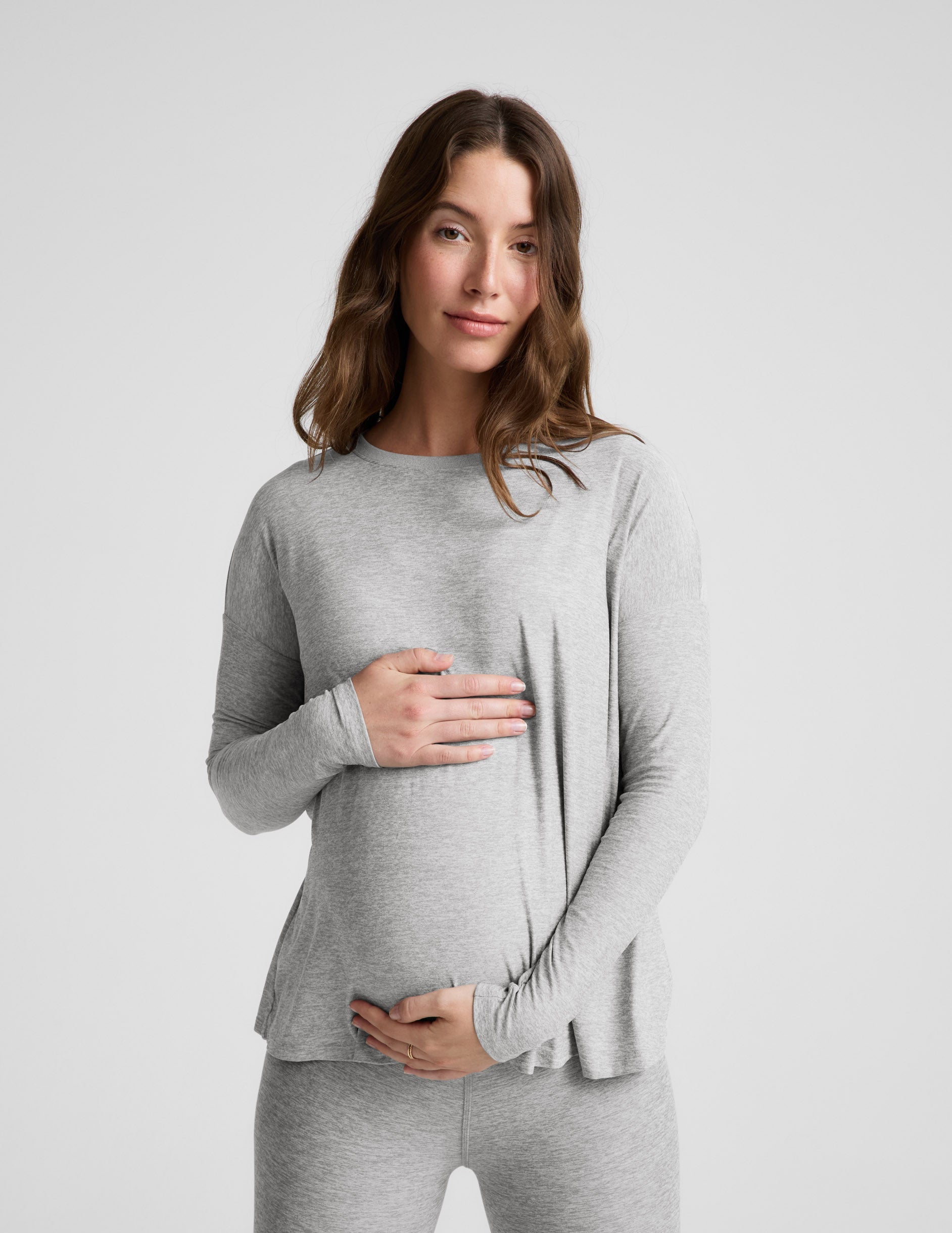 Pregnant woman wearing a gray long-sleeve top and leggings on a white background.