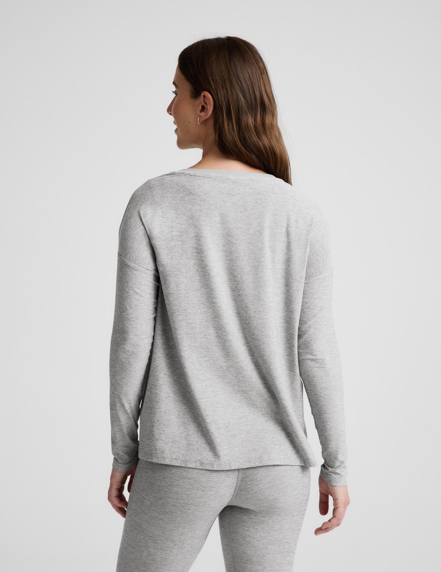 Pregnant woman wearing a gray long-sleeve top and leggings on a white background.