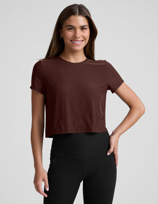 Woman wearing a brown cropped t-shirt and black bootcut pants against a plain background.