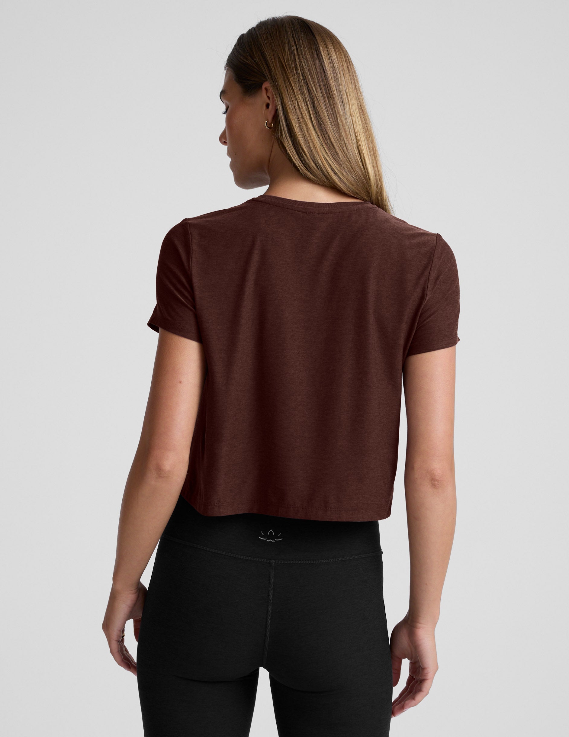 Woman wearing a brown cropped t-shirt and black bootcut pants against a plain background.