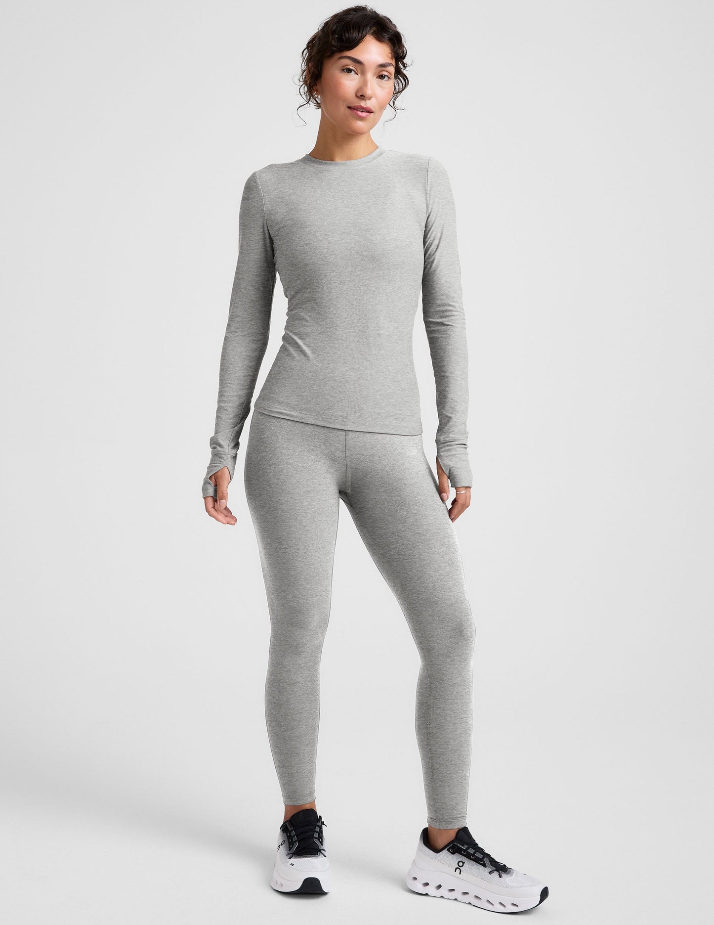 model wearing a fitted gray long-sleeve crew neck top and leggings on a light gray background.