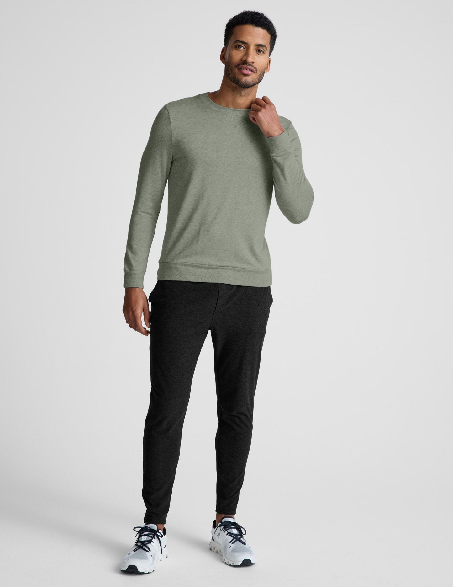 Man wearing a green long-sleeve shirt and black pants on a light gray background.