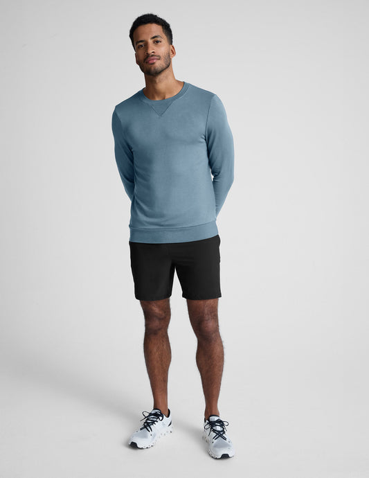 Man wearing a blue sweater and black shorts on a white background.