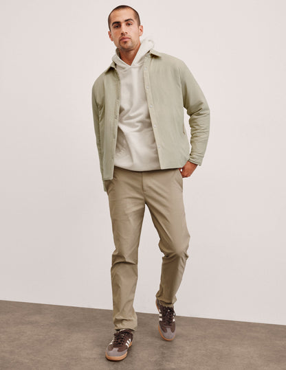 man wearing a light jacket and beige chino pants against a plain background.