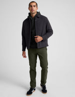 Man wears olive green Essential Men's Chino 30" Trouser with a straight-leg fit, black jacket, and sneakers.