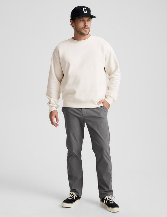 A man wears gray Element Men's Chino Trouser 30" in a slim straight fit with a cream sweatshirt and black baseball cap.