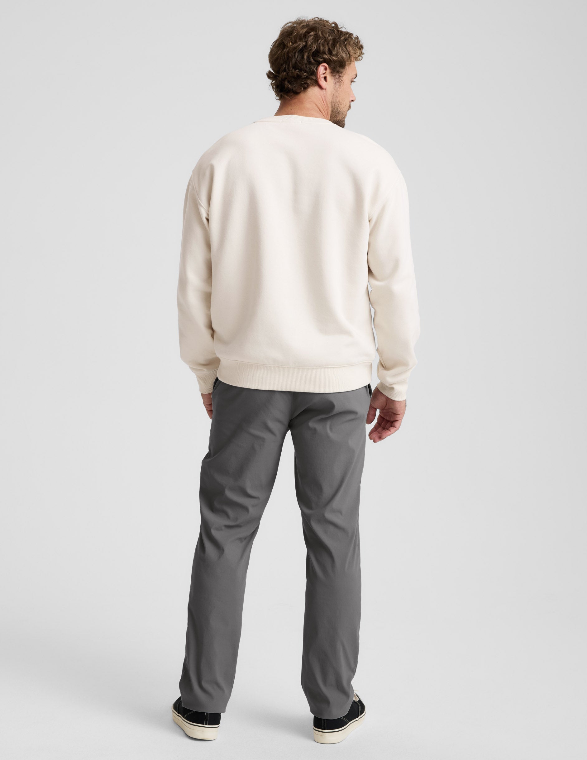 Rear view of a man wearing Element Men's Chino Trousers in dark gray, styled with a cream sweatshirt and black sneakers.