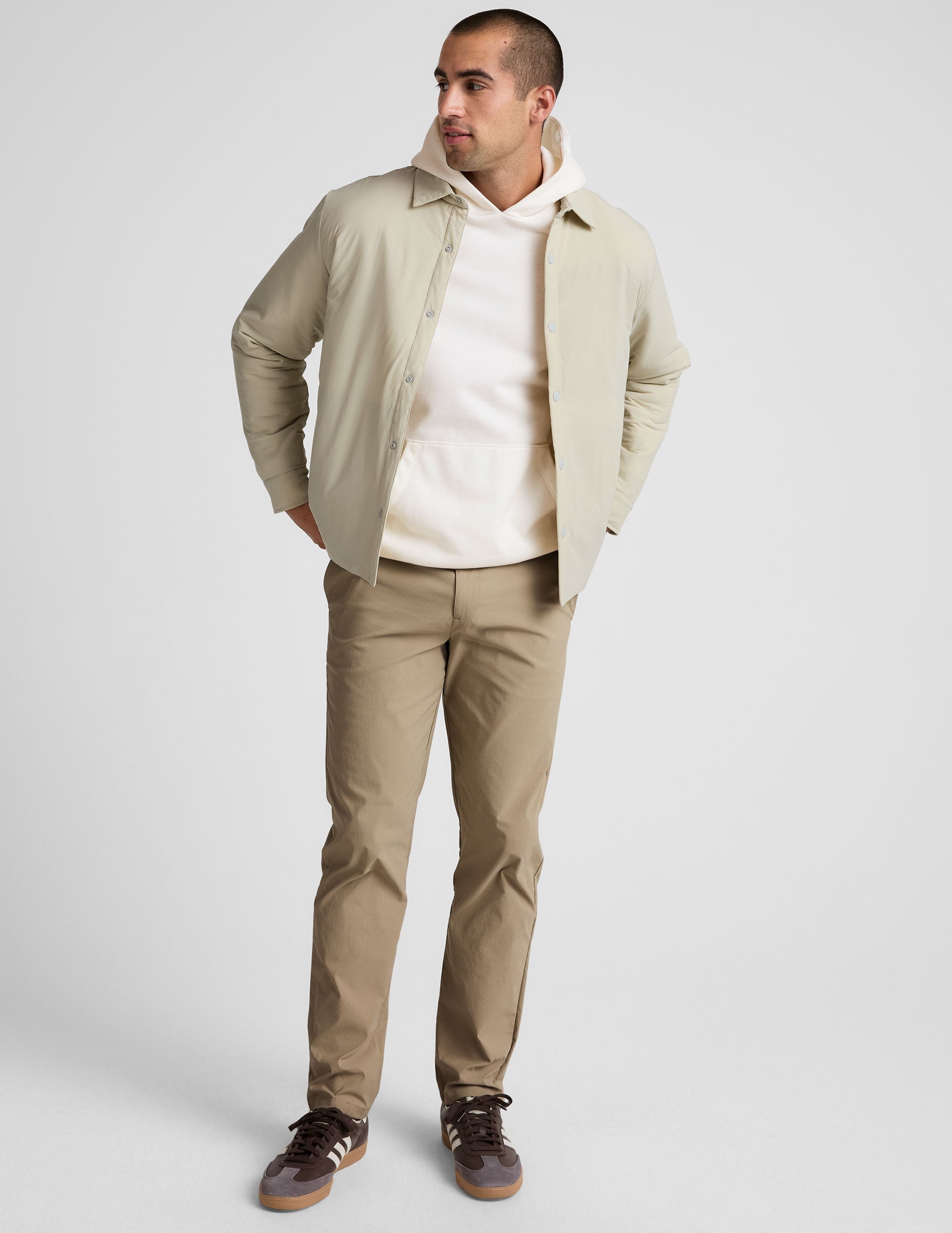 Man wearing beige Essential Men's Chino 32" Trouser, a straight-leg pant styled with a hoodie and jacket in a full-body view.