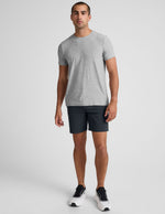 A man wearing dark grey Essential Men's Chino 7" Shorts, a grey t-shirt, and sneakers against a white background.