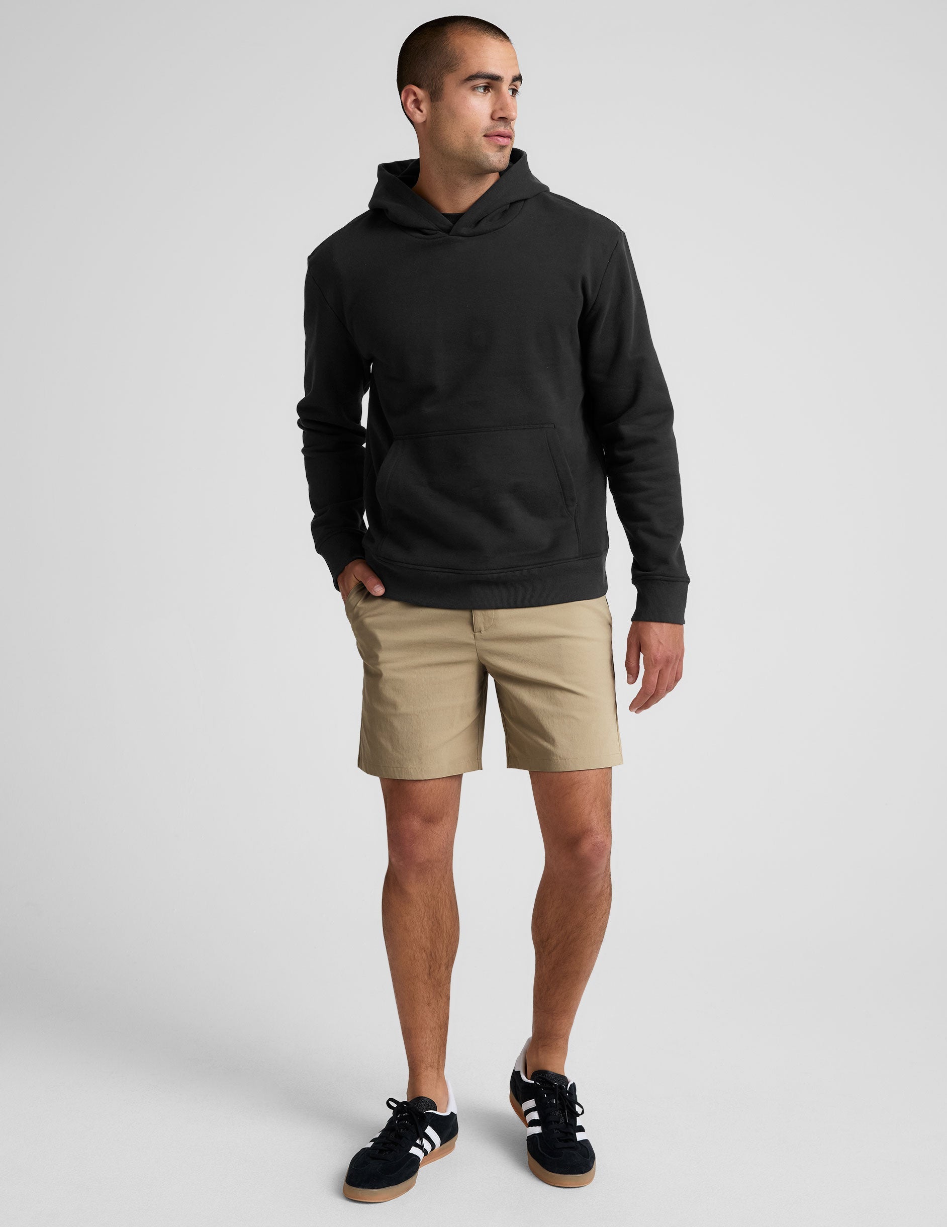 Front view of a man wearing beige Essential Men's Chino 7" Short with a 7-inch inseam, black hoodie, and black sneakers.