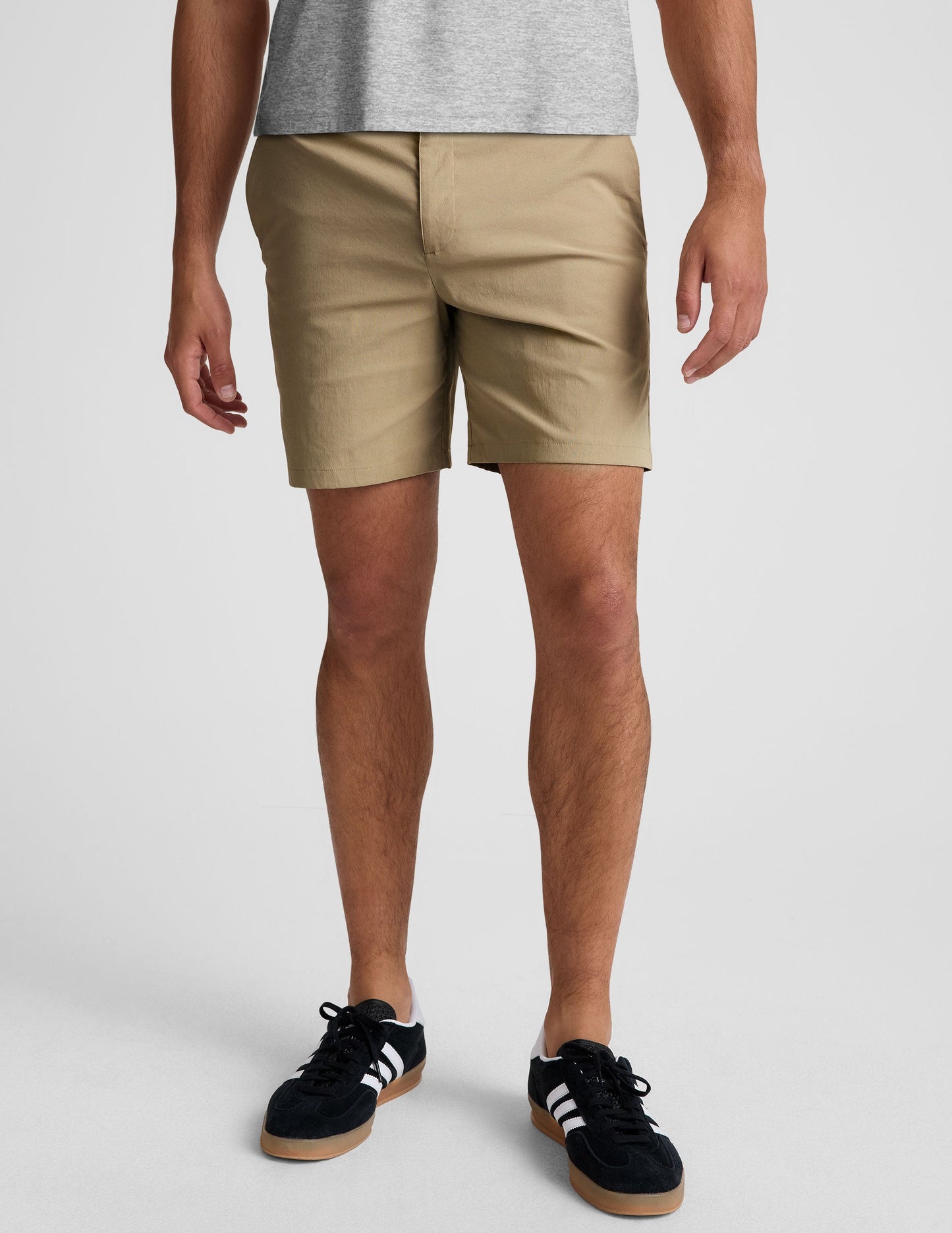 Front view of beige Essential Men's Chino 7" Short with button closure, belt loops, and side pockets on a model.