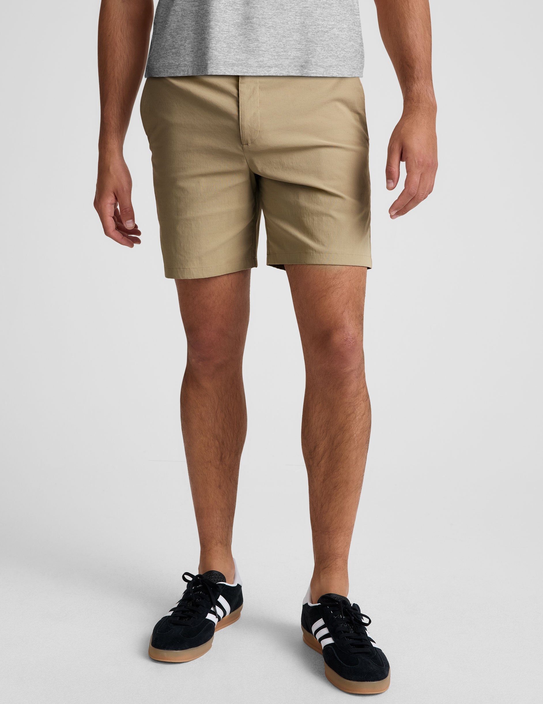 Front view of beige Essential Men's Chino 7" Short with button closure, belt loops, and side pockets on a model.