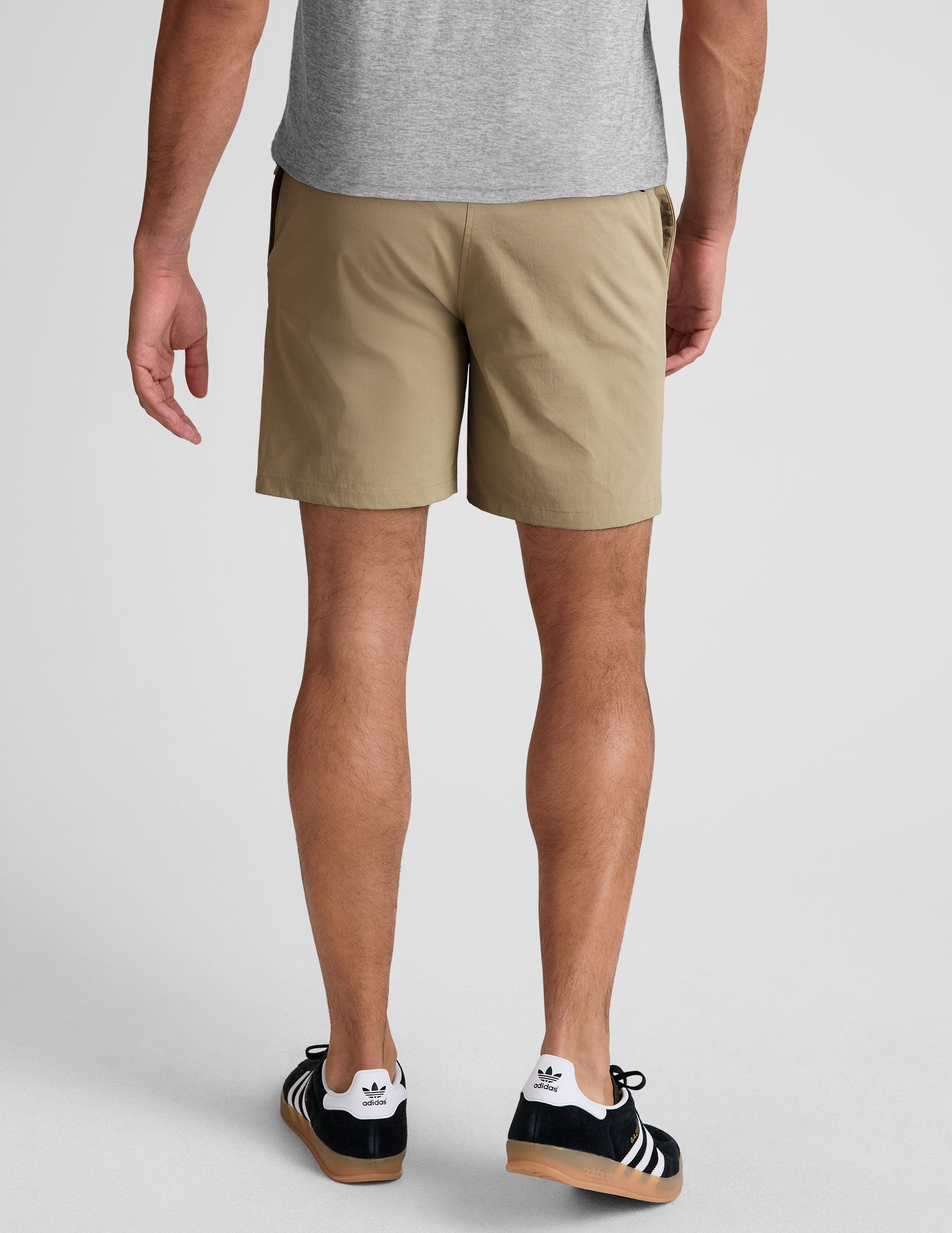 Rear view of a man wearing beige Essential Men's Chino 7" Short featuring belt loops and back zippered welt pockets.