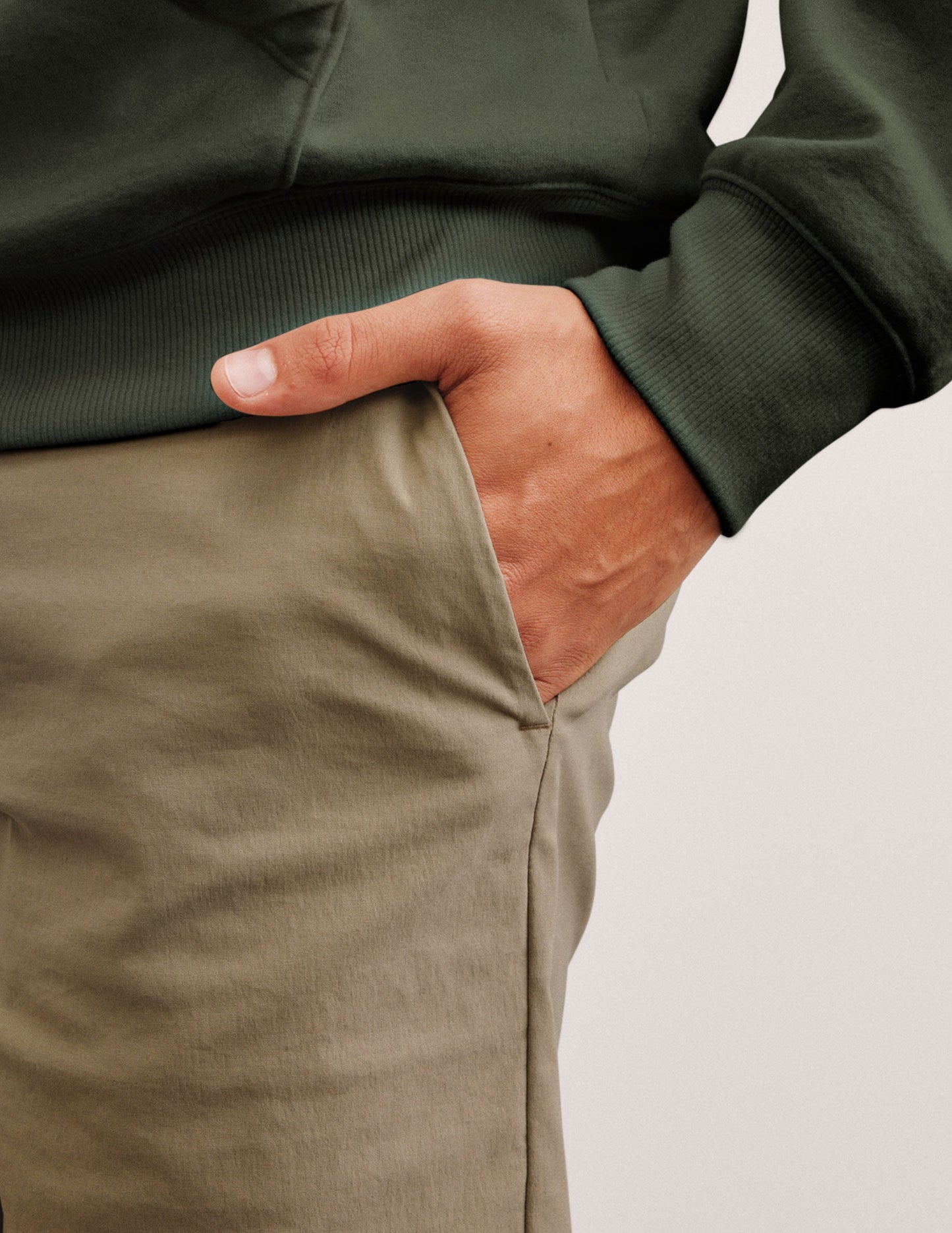 man wearing a green hoodie and beige chino shorts with pockets standing against a plain background.