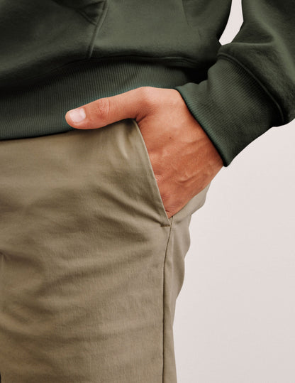 man wearing a green hoodie and beige chino shorts with pockets standing against a plain background.