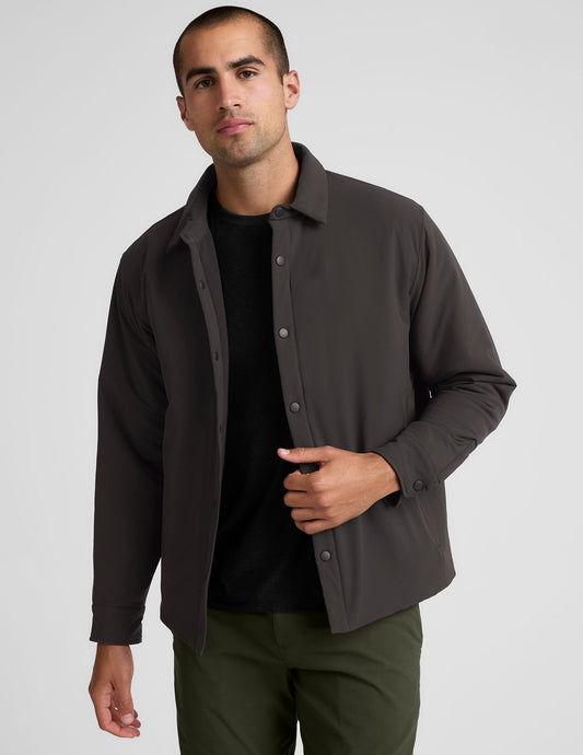 Man wearing a dark brown jacket over a black shirt with green pants on a light gray background.