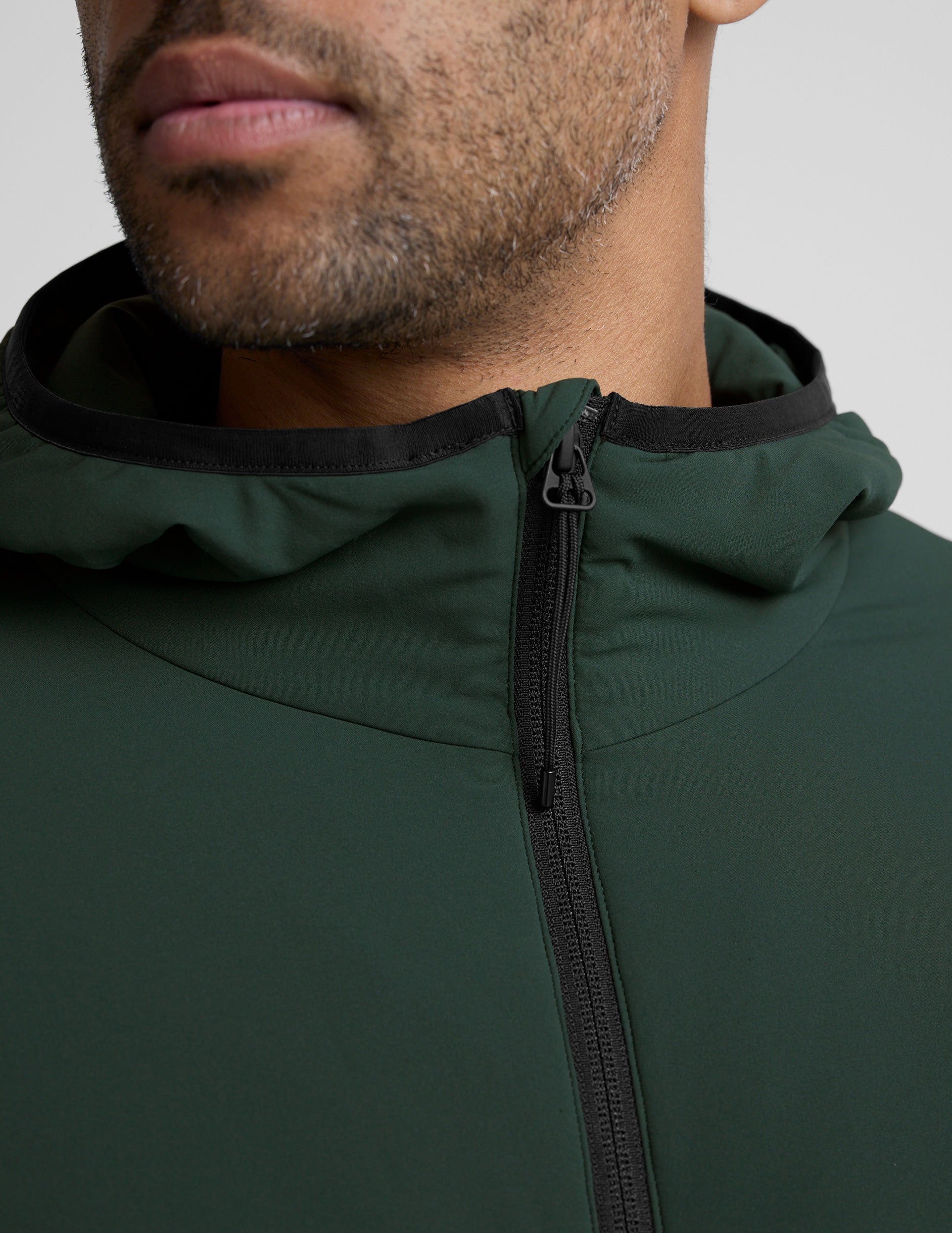 man wearing a green jacket with a hood on a gray background.