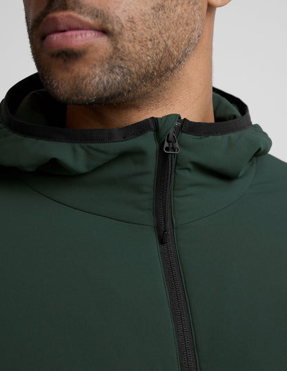 man wearing a green jacket with a hood on a gray background.