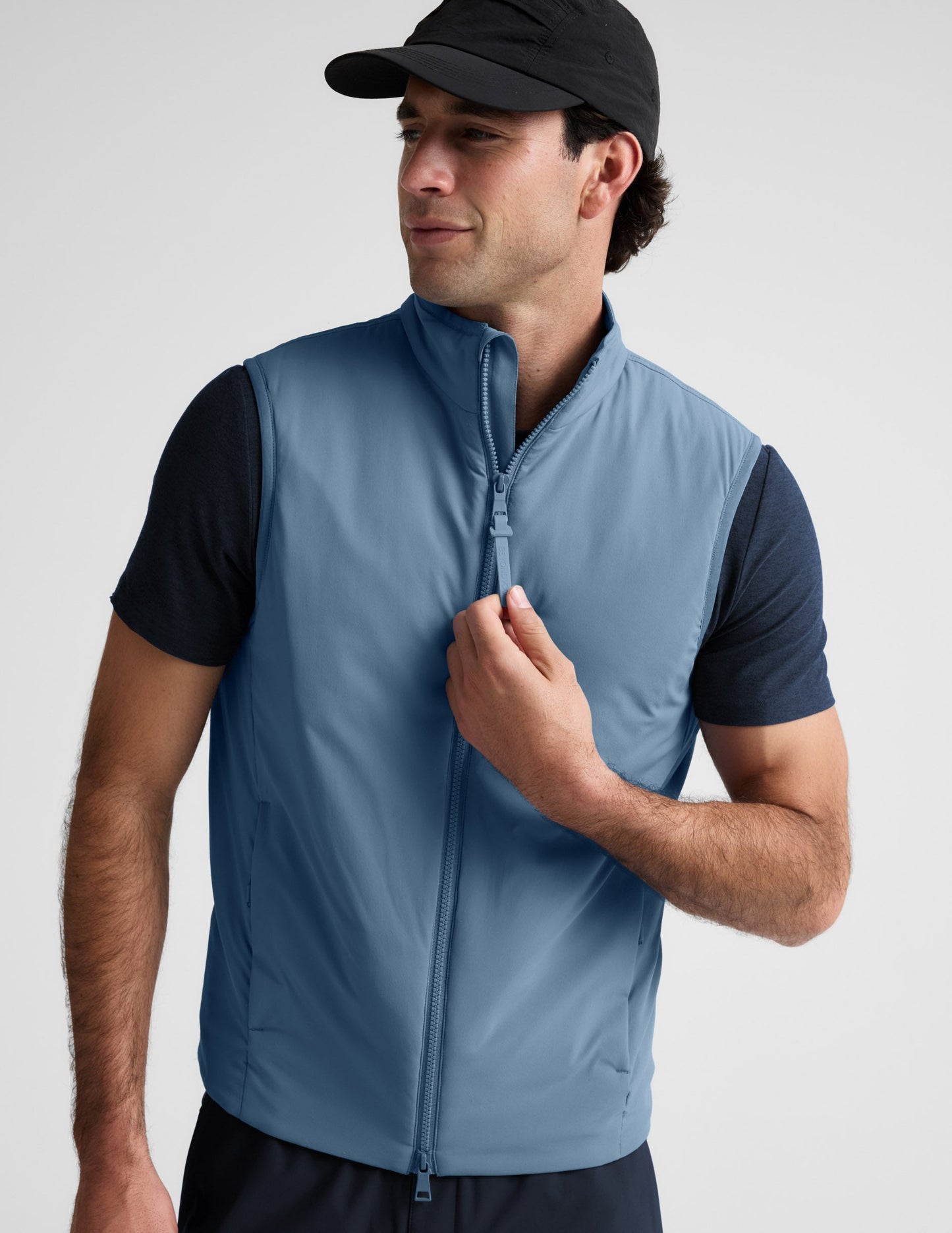 Man wearing a light blue vest over a black shirt on a plain background.