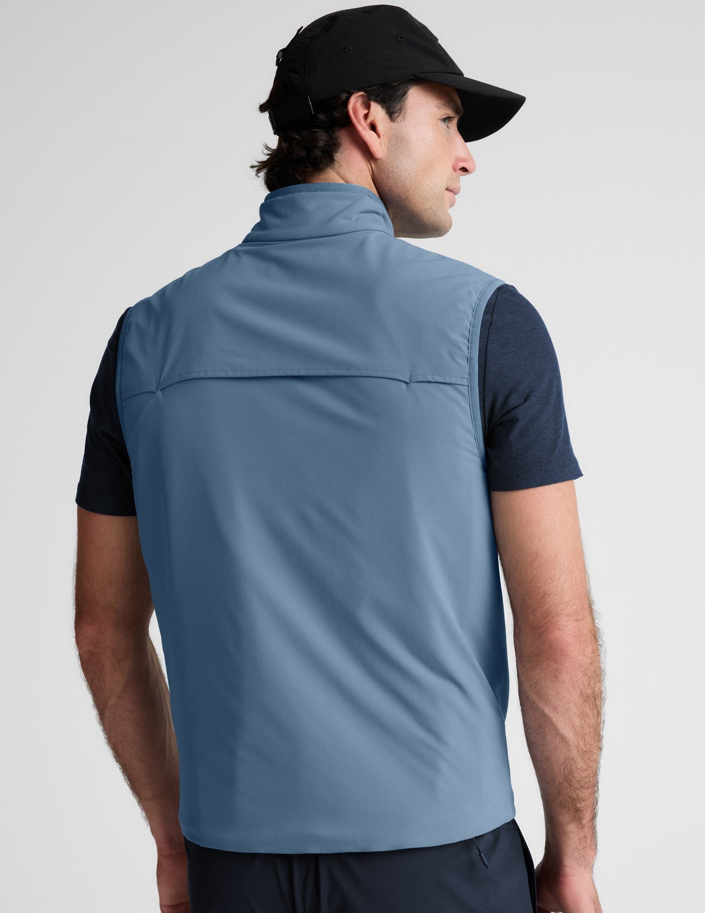 Man wearing a light blue vest over a black shirt on a plain background.