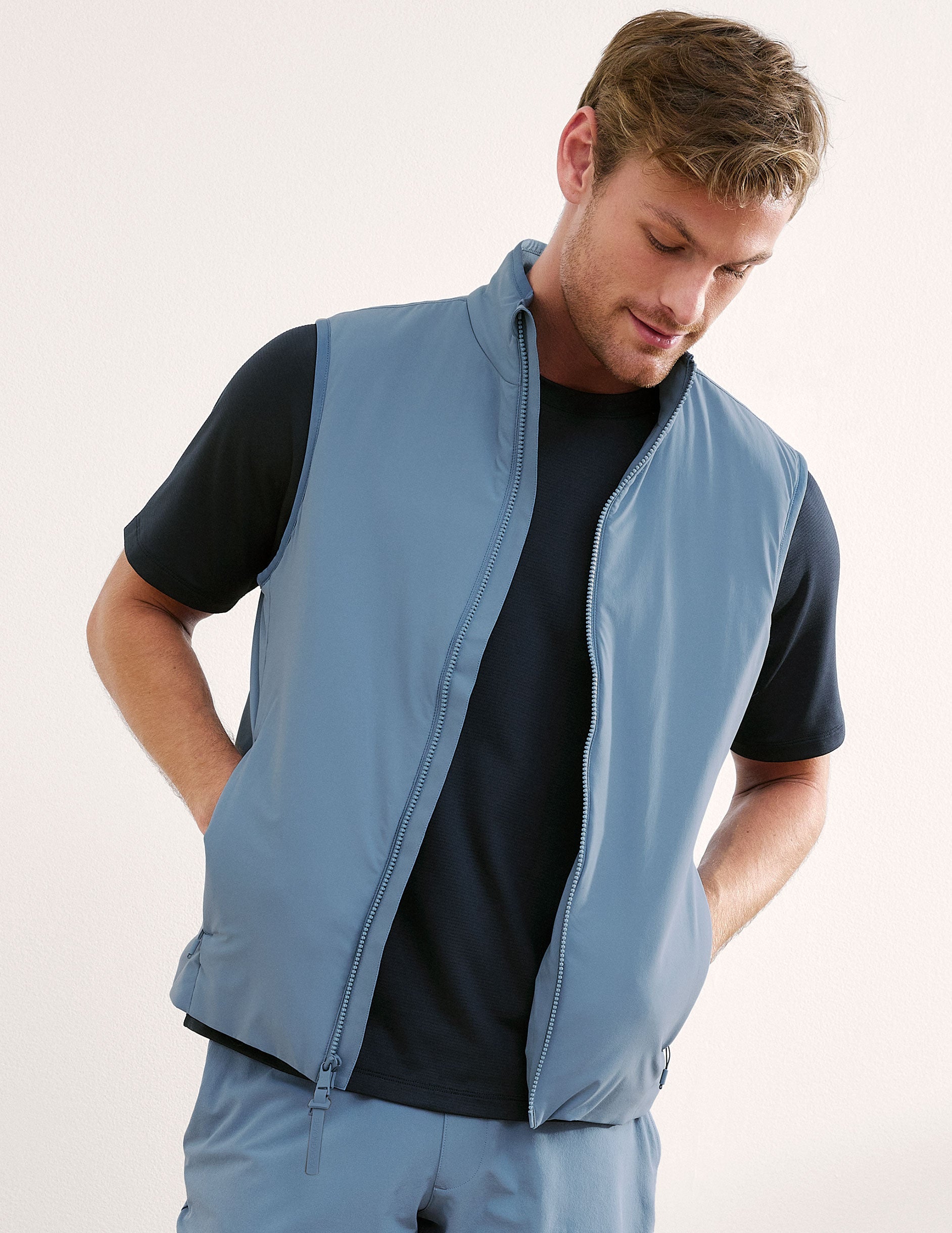 Man wearing a light blue vest over a black shirt on a plain background.