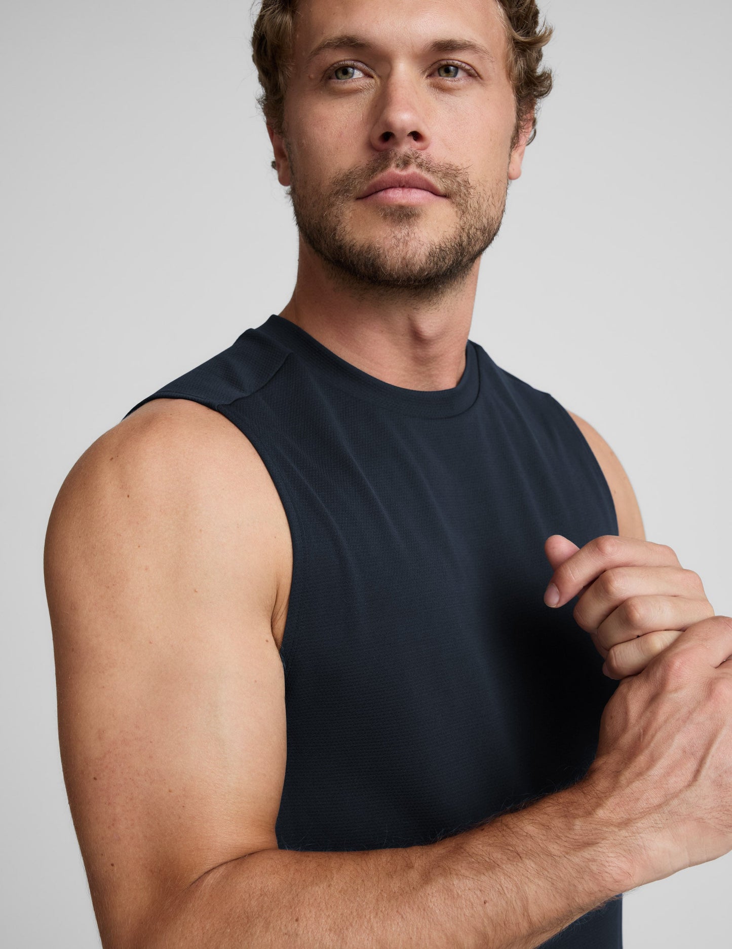 Man wearing a blue sleeveless shirt and black shorts against a light background.