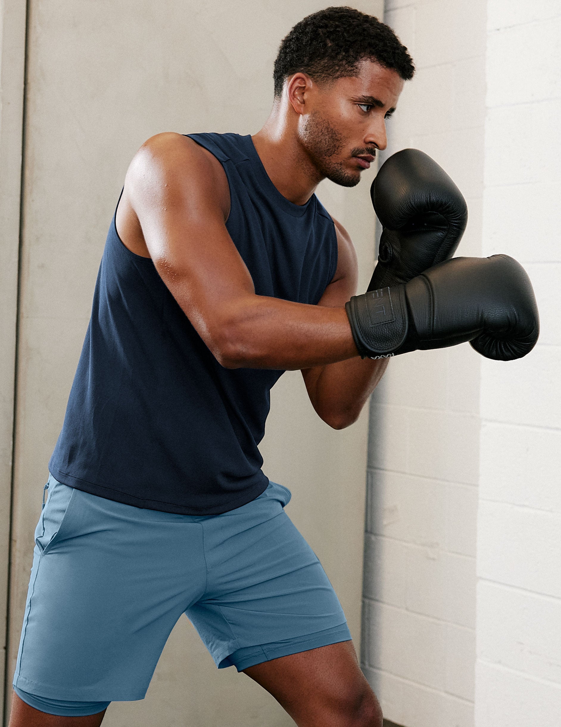 Man in a blue athletic tank and blue shorts with boxing gloves.