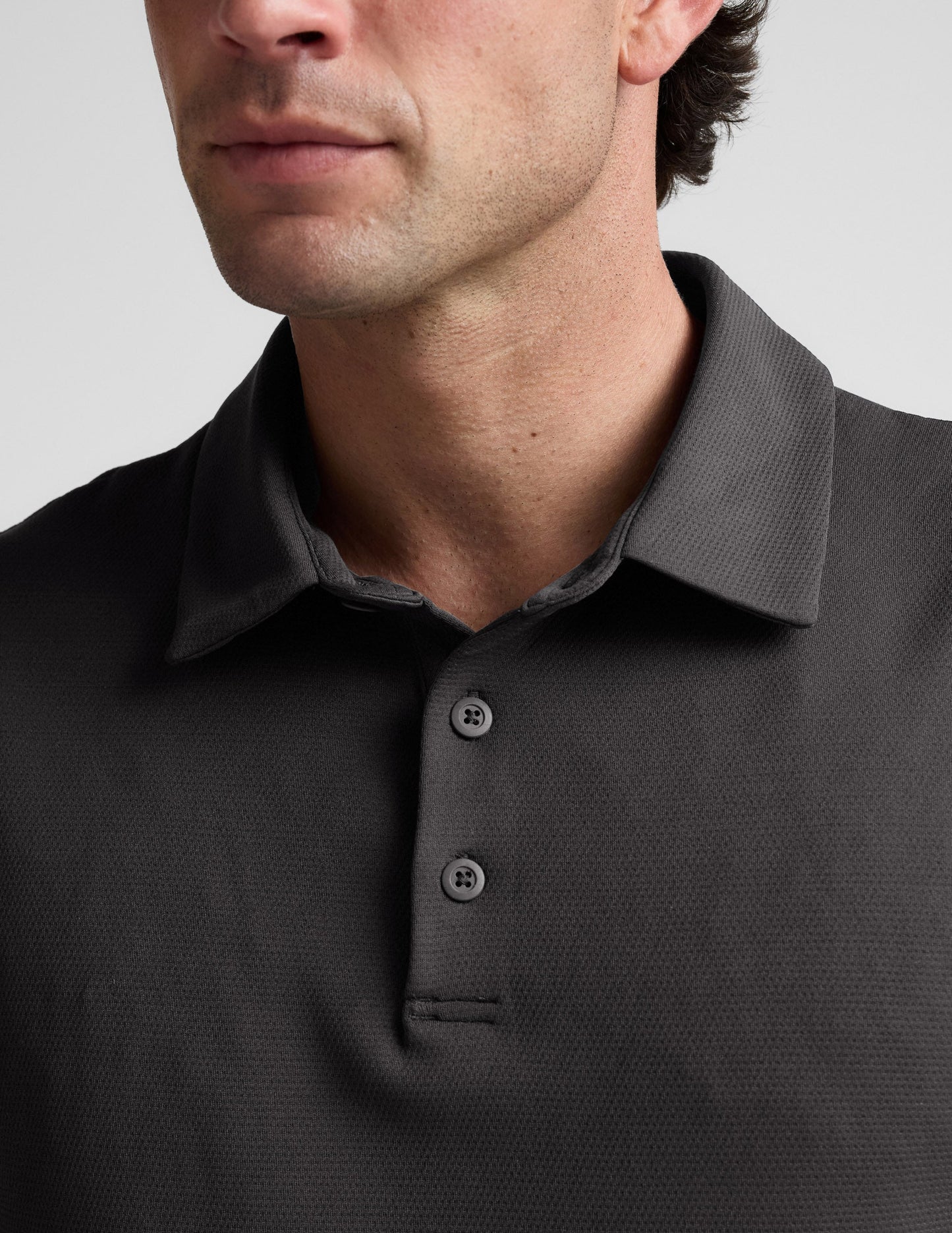 Man wearing a dark gray polo shirt against a light gray background.